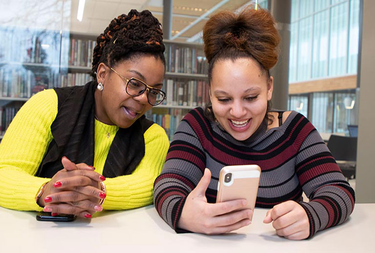 Two peaople seated at a table looking at a smart phone screen.